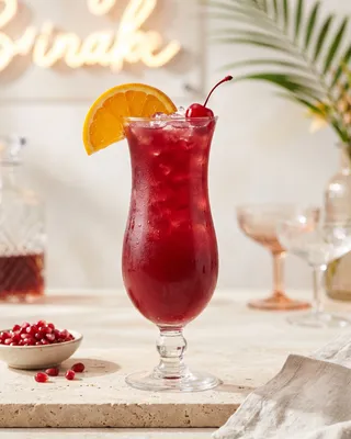 Hurricane in a hurricane glass with orange and a cocktail cherry