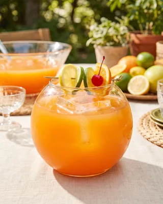 Whiskey Sour Punch in a fishbowl glass with lemon, lime, orange and a cocktail cherry