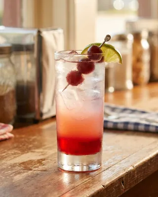 Dirty Shirley in a highball glass with cocktail cherries and lime